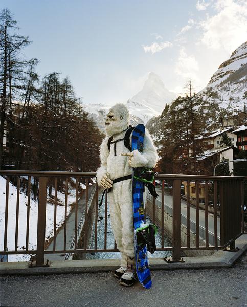 A snowboarder in a white ape costume poses in Zermatt, Switzerland with the Matterhorn rising in the background.